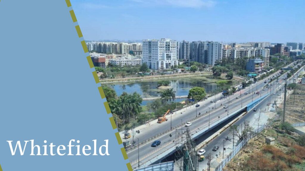 Aerial view of Whitefield showcasing a mix of residential buildings, a body of water, and a main road with traffic, surrounded by projects from house construction companies in Bangalore.