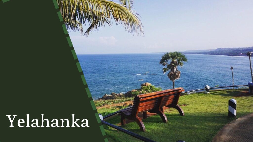 A wooden bench overlooks a coastal landscape with lush greenery and the ocean in the background. The text "Yelahanka" appears on the left side of the image, reminding one of the serene locations house construction companies in Bangalore often capitalize on.